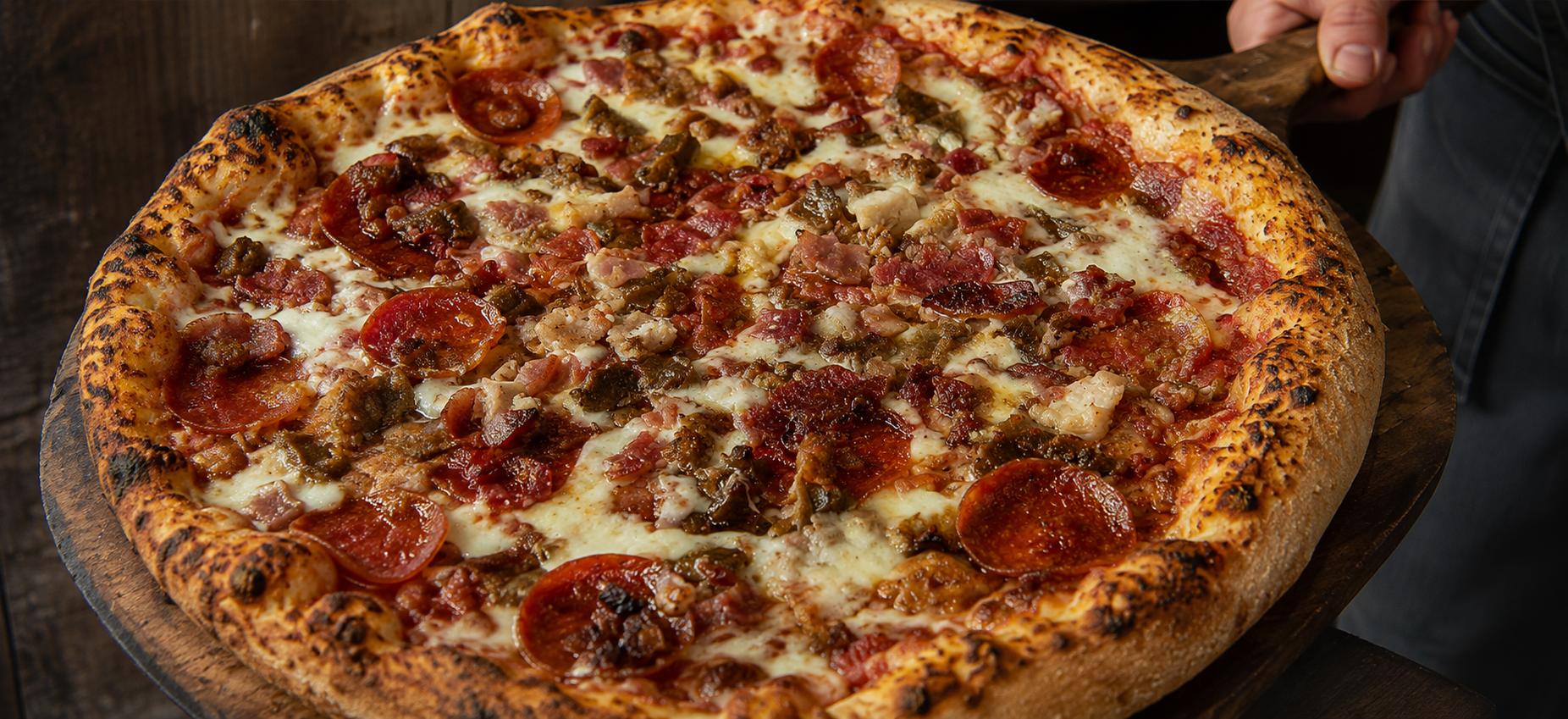 A handcrafted meat-lovers pizza fresh out of the oven on a wooden peel.